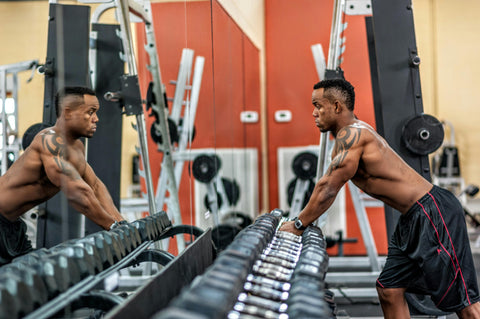 man looking in mirror about to pick up barbell in the gym